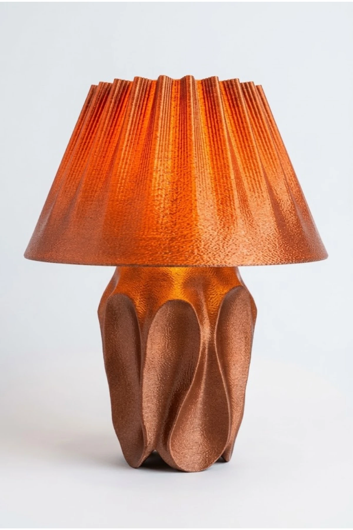 Aura Copper Red masa lambası, kızıl bakır pilili başlık ve dalgalı gövdeyle açık gri stüdyo zemininde