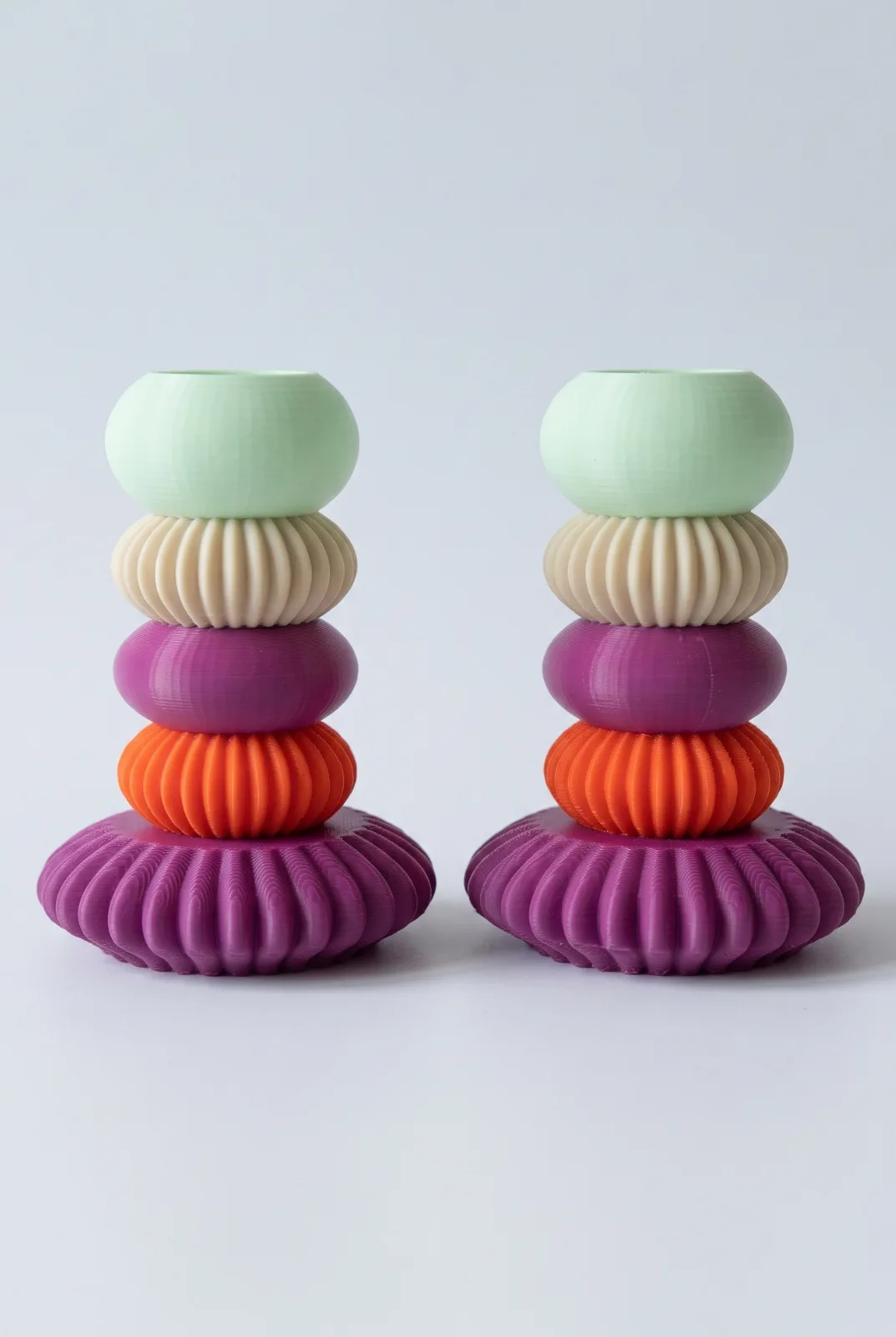 Mint, bej, mor ve turuncu halkalı iki MACARON şamdan, açık zeminde stüdyo çekimi